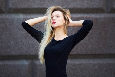 Siyah elbiseli çekici sarışın. Taş bir duvarın arkasında.