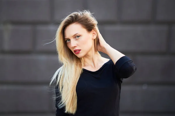 Attraktive Blondine im schwarzen Kleid. vor dem Hintergrund einer Steinmauer. — Stockfoto