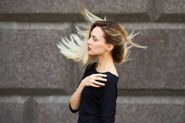 Sexig blond tjej i svart klänning. Med flygande hår mot en stenmur. — Stockfoto