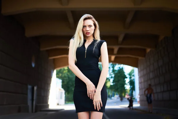 Schöne Blondine in einem schwarzen kurzen Kleid. schaut in den Rahmen. im Bogen unter der Brücke. — Stockfoto
