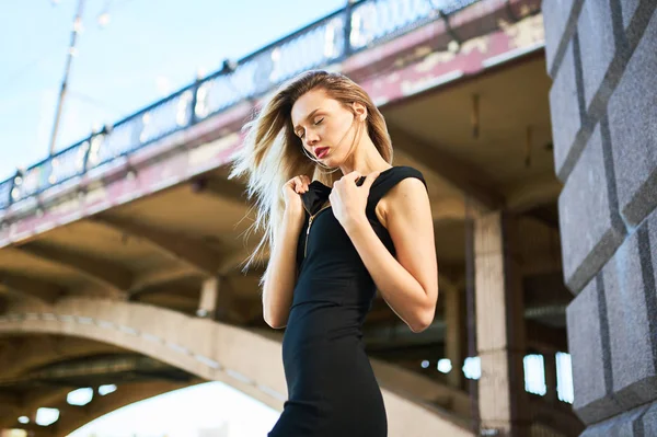 Sexig blond tjej i svart klänning. Mot bakgrund av en välvd bro. — Stockfoto