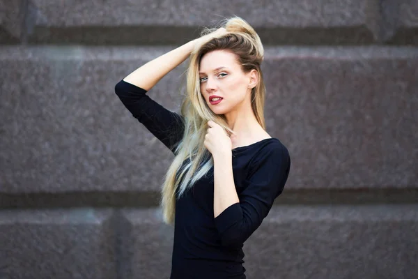 Snygg blondin i svart klänning. Mot bakgrund av en stenmur. — Stockfoto