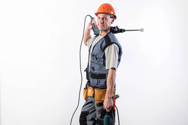 Um construtor com uma broca de martelo no ombro, com um capacete, sorri . — Fotografia de Stock