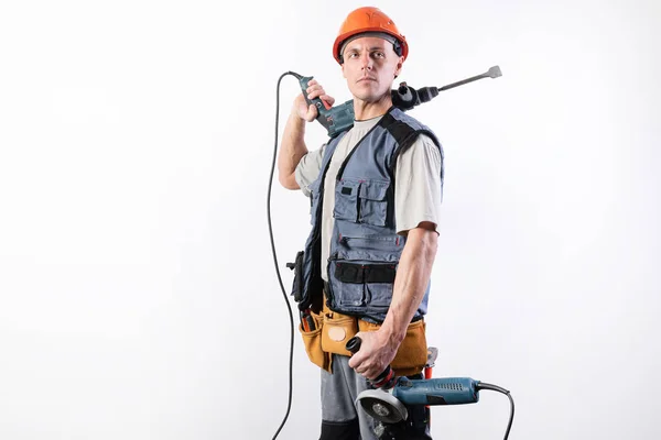 Un constructor con un taladro de martillo en su hombro, y una amoladora angular en su otra mano, en un casco, sonríe . — Foto de Stock