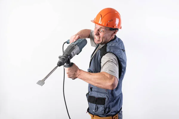 Um construtor com uma expressão engraçada, num capacete, com um perfurador . — Fotografia de Stock