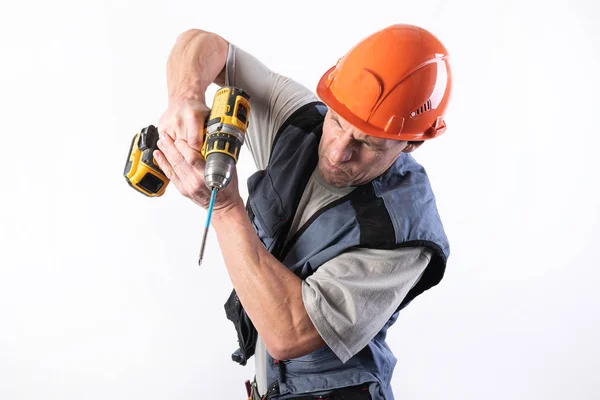 Construtor com uma expressão engraçada, em um capacete, com uma broca sem fio . — Fotografia de Stock