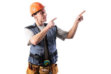 İnşaatçı sağı işaret ediyor. İşaret parmaklarıyla teklif ediyor. İş kıyafetleri ve şapkayla..