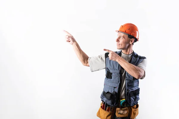 O construtor aponta para a esquerda. Oferece com dedos indicadores. Em roupas de trabalho e chapéu duro . — Fotografia de Stock