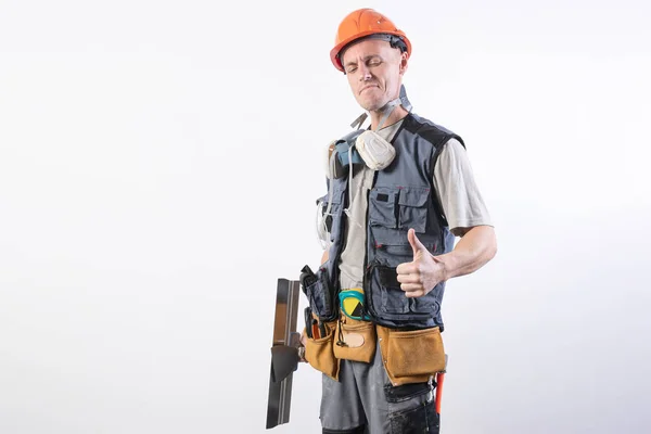 Constructor con espátula. Y mostrando los pulgares hacia arriba. Con ropa de trabajo y sombrero duro. Sobre un fondo gris claro . — Foto de Stock