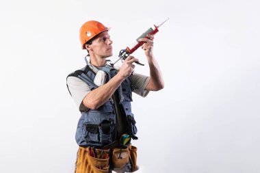 Mühürlü bir inşaatçı. İş kıyafetleri ve şapkayla. Açık gri bir arkaplanda.