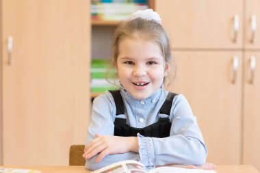 Liseli kız kitaplarla bir masada oturuyor ve gülümsüyor..