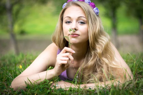 Schöne blonde Mädchen. auf dem Gras liegen und eine Blume riechen. — Stockfoto