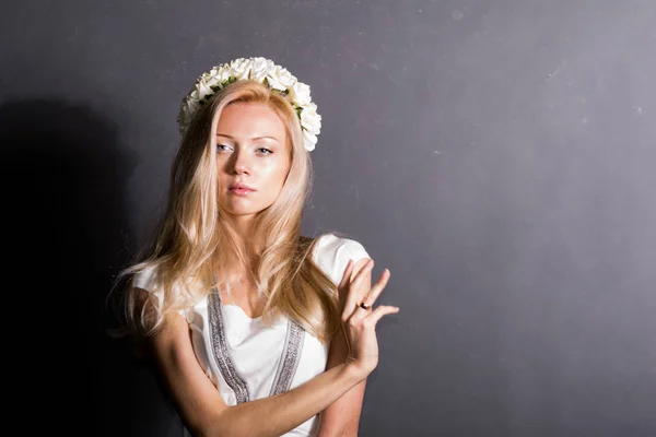 Schöne blonde Mädchen im Studio. in einem weißen Kleid, auf dunklem Hintergrund. — Stockfoto
