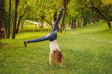 Kız akrobatik tekerlek yapıyor. Çimlerin üzerinde.