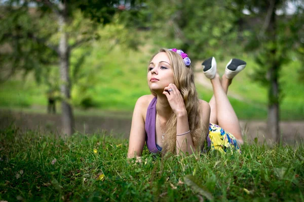 Schönes blondes Mädchen, liegt im Gras, schaut verträumt zur Seite. — Stockfoto