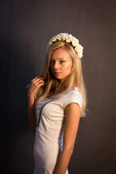 Vacker blond tjej i studion. I en vit klänning, på en mörk bakgrund. — Stockfoto