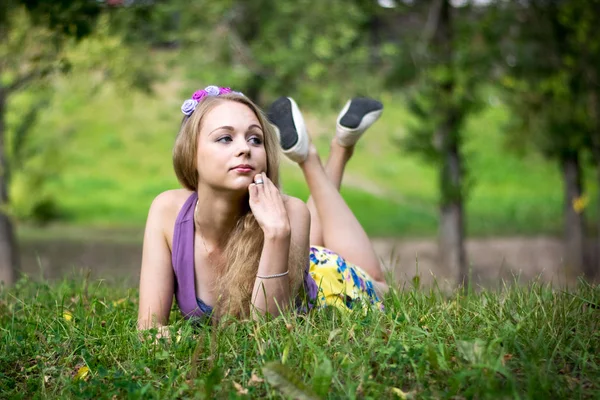 Güzel sarışın kız. Çimlere uzanıp dikkatlice yan tarafa bakıyor.. — Stok fotoğraf