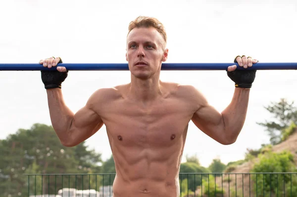 De gespierde man trekt zich omhoog op de dwarsbalk. In de open lucht. — Stockfoto