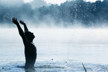 Suda kemer takmış bir adam, kenarlara su sıçratıyor. Sis ile.