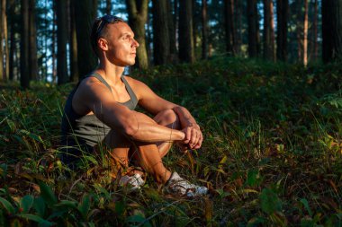 Ormanda gün batımında dinlenen atletik bir adam..
