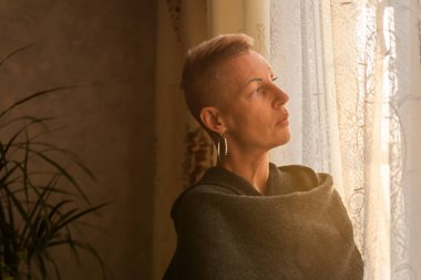 Pencere kenarında kısa saçlı, yetişkin bir kadın..