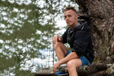 Bir gölün kıyısında, bir ağacın köklerinde oturan bir adam. Herhangi bir amaç için.