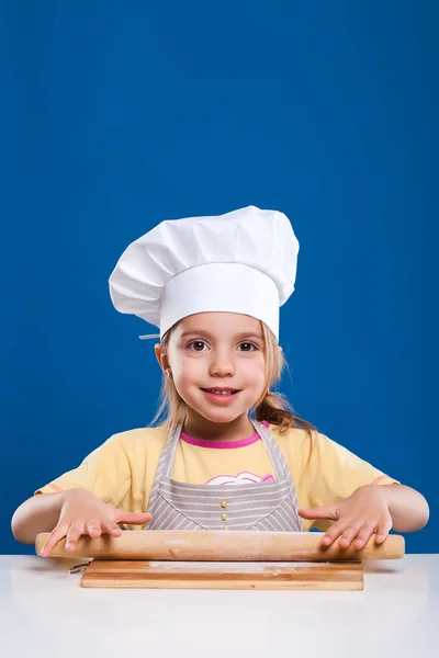 Das kleine Mädchen kocht und bereitet Essen auf blauem Hintergrund zu — Stockfoto