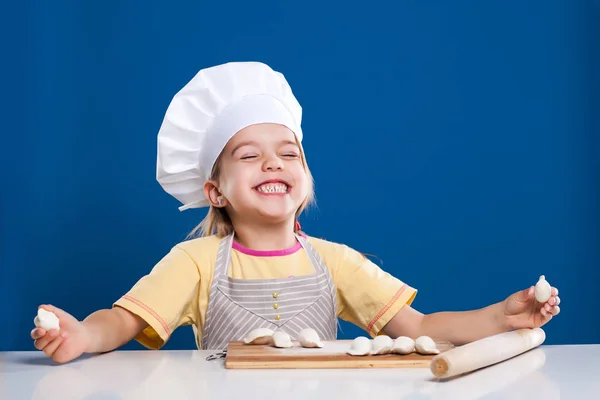 Das kleine Mädchen kocht und bereitet Essen auf blauem Hintergrund zu — Stockfoto