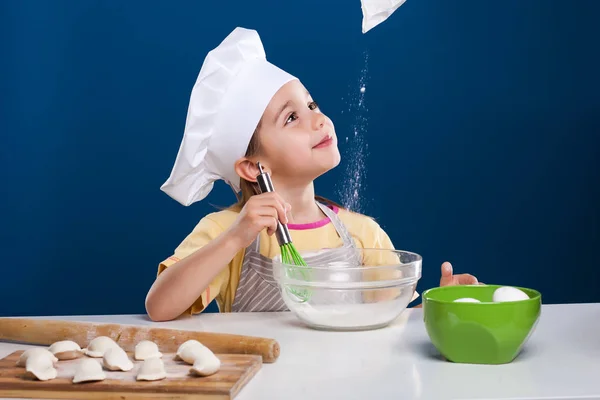 Das kleine Mädchen kocht und bereitet Essen auf blauem Hintergrund zu — Stockfoto