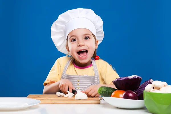 Das kleine Mädchen bereitet Salat auf blauem Hintergrund zu — Stockfoto