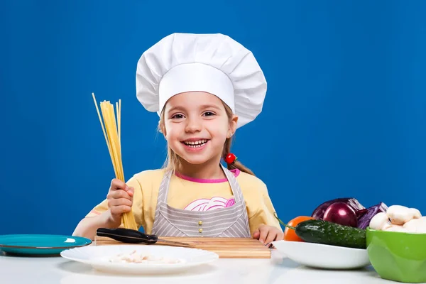 Das kleine Mädchen bereitet Essen auf blauem Hintergrund zu — Stockfoto