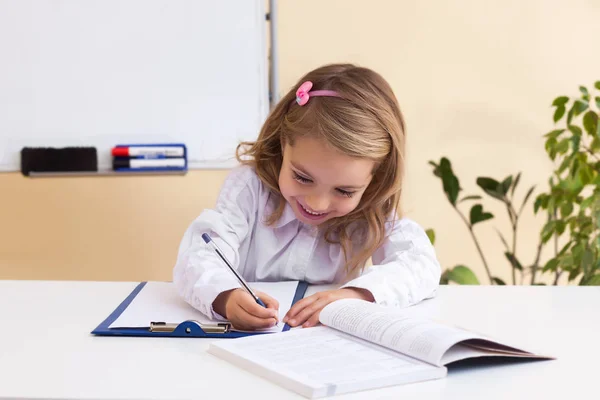 Menina bonita escreve sentado à mesa — Fotografia de Stock