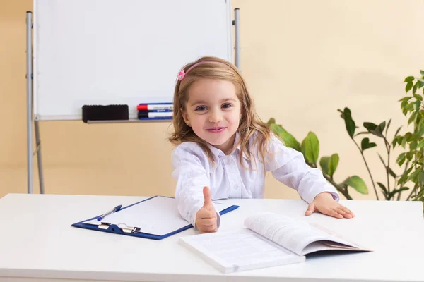 Hermosa niña escribe sentado en la mesa —  Fotos de Stock