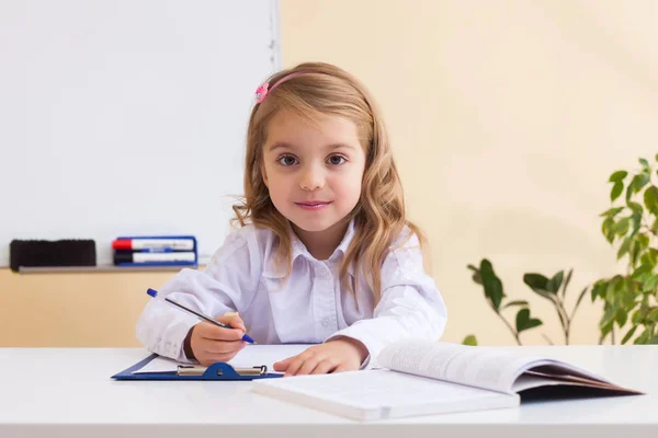 Красивая маленькая девочка пишет сидя за столом — стоковое фото