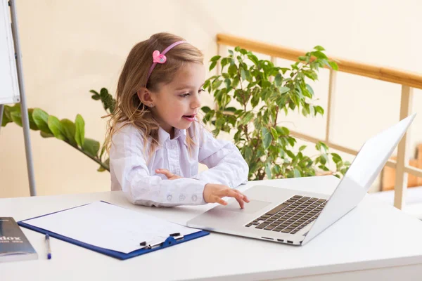 Hermosa niña está sentada en la mesa con el ordenador portátil —  Fotos de Stock
