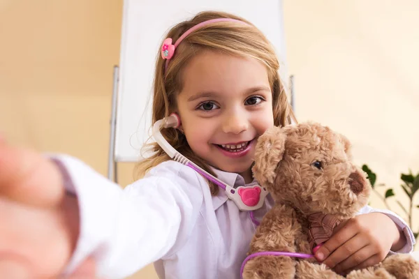 Маленькая девочка лечит игрушечного медведя и делает селфи — стоковое фото