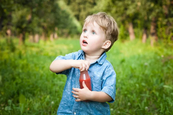 Little boy walks alone in a meadow and drinks juice