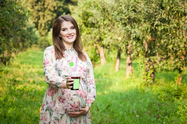 Pregnant woman walks alone in a meadow and drinks juice