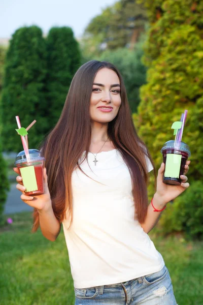 Красивая молодая девушка пьет и делится соком в саду — стоковое фото