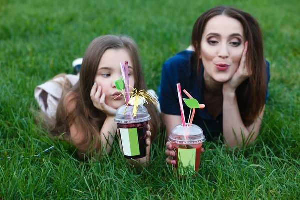 Mamãe e filha estão deitados em um prado e bebendo suco — Fotografia de Stock