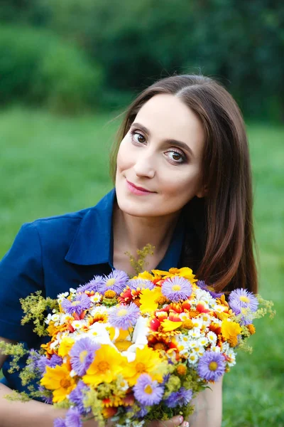 Mulher em um vestido azul está sentado em um prado com flores — Fotografia de Stock