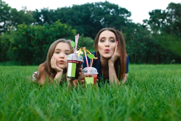 Mamãe e filha estão deitados em um prado e bebendo suco — Fotografia de Stock