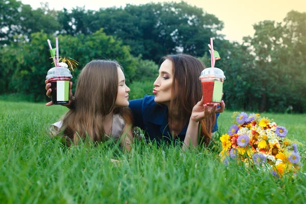 Mamãe e filha estão deitados em um prado e bebendo suco — Fotografia de Stock