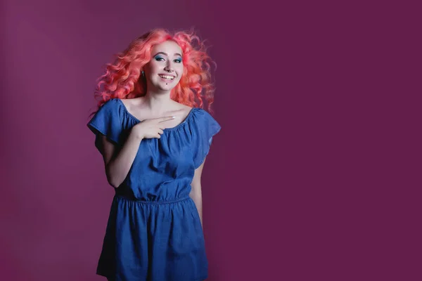 Hermosa chica con el pelo rosa en vestido azul muestra signo sobre fondo lila, lugar para el texto — Foto de Stock