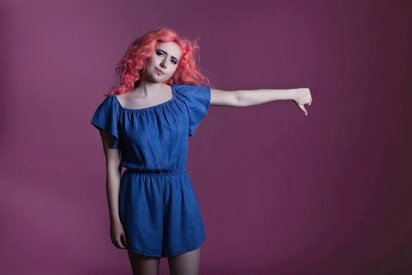 Hermosa chica con el pelo rosa en vestido azul muestra signo sobre fondo lila, lugar para el texto — Foto de Stock