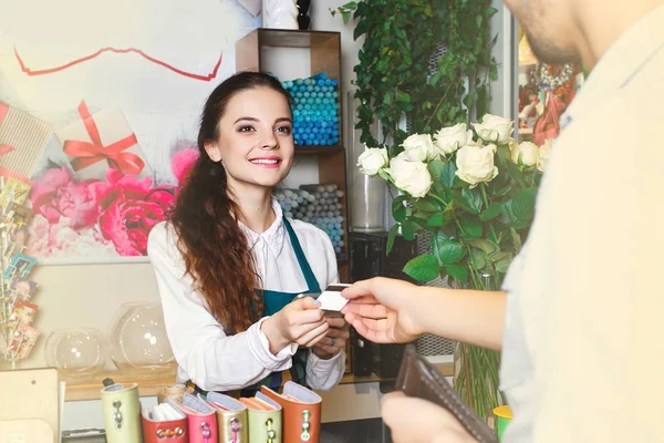 Mujer joven trabajando como florista dando tarjeta de crédito al cliente —  Fotos de Stock