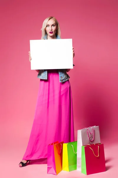 Winkelen vrouw met boodschappentassen op roze achtergrond. Houdt van een witte naamplaatje voor uw tekst — Stockfoto