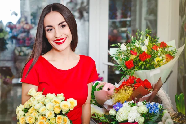 Hermosa morena en vestido rojo compra un ramo de flores en una florería — Foto de Stock