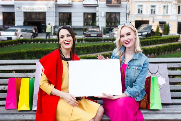 Concetto di gente felice - belle donne con borse della spesa. Tenere una targhetta bianca per il testo Fotografia Stock