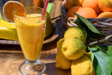 Portakal ve limon tablosunun yanındaki bir cam fincan taze sıkılmış portakal suyu yatıyor